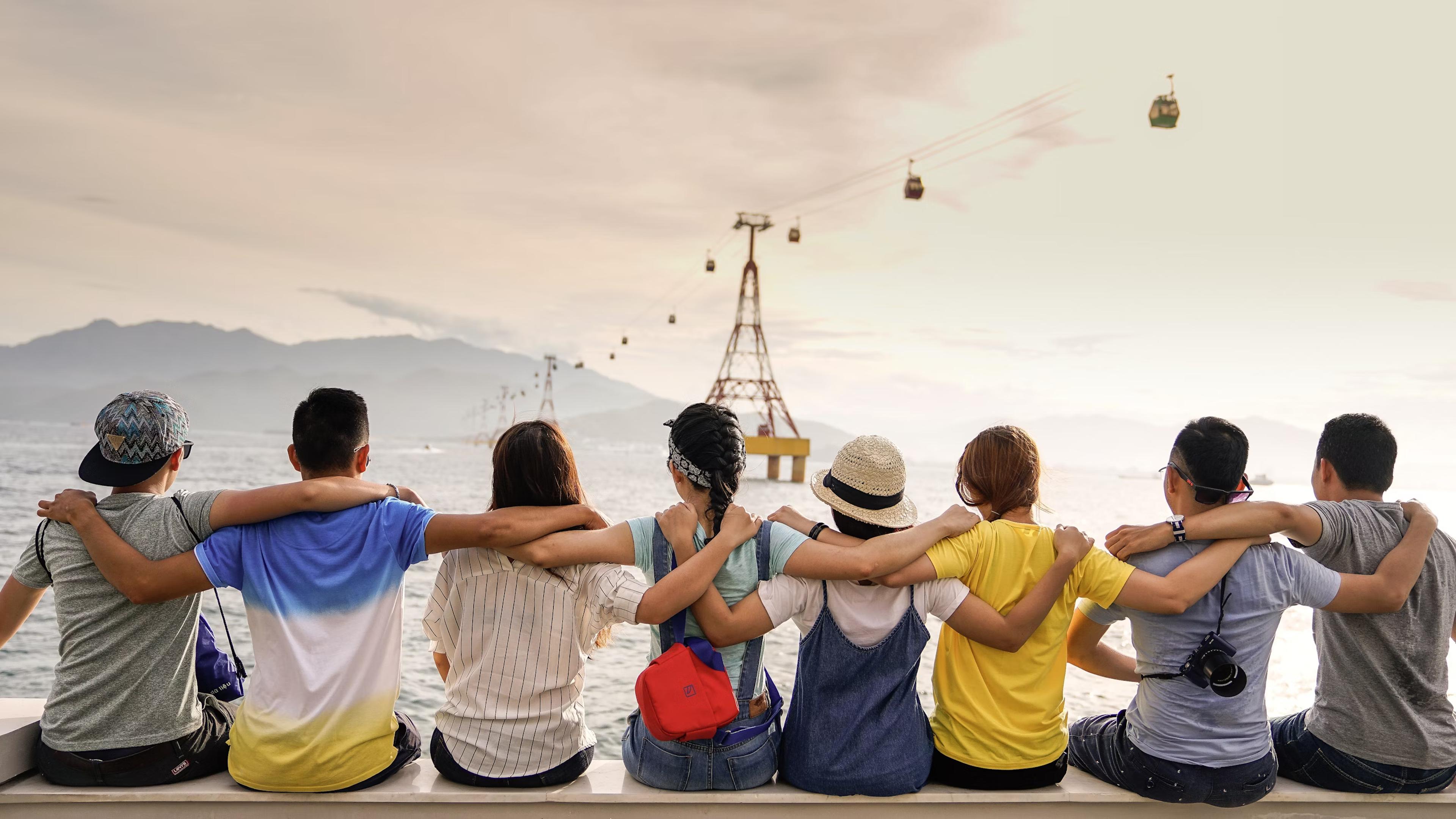 Group of friends hands over shoulders looking out into the ocean.